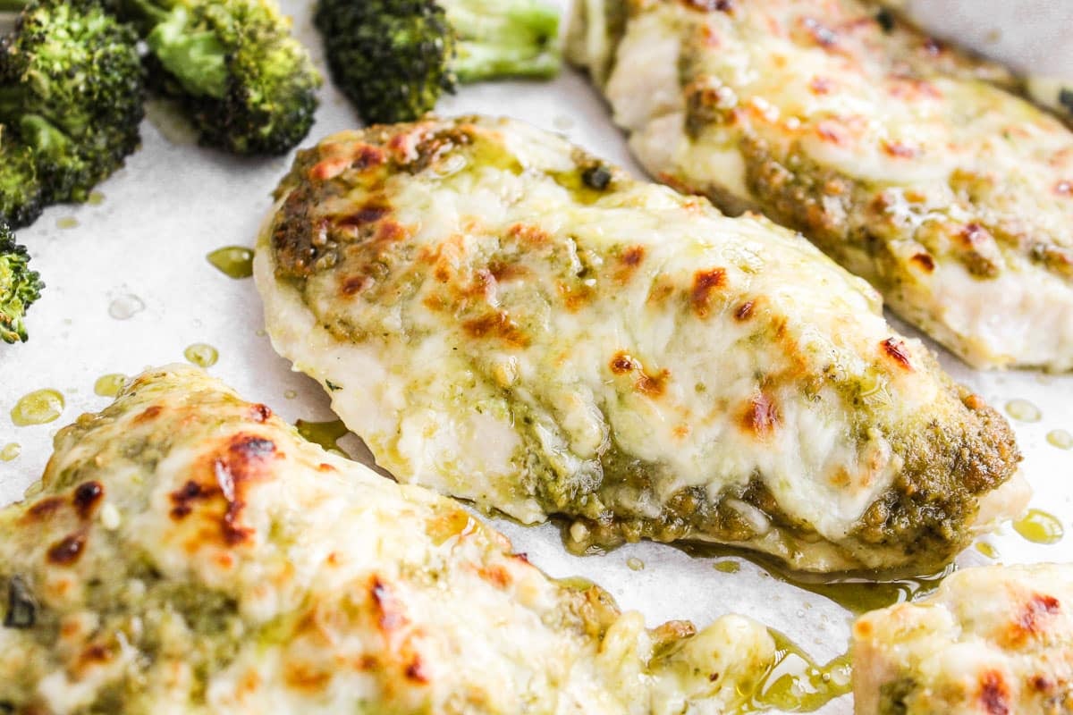 Chicken breasts covered in pesto and mozzarella on a baking sheet